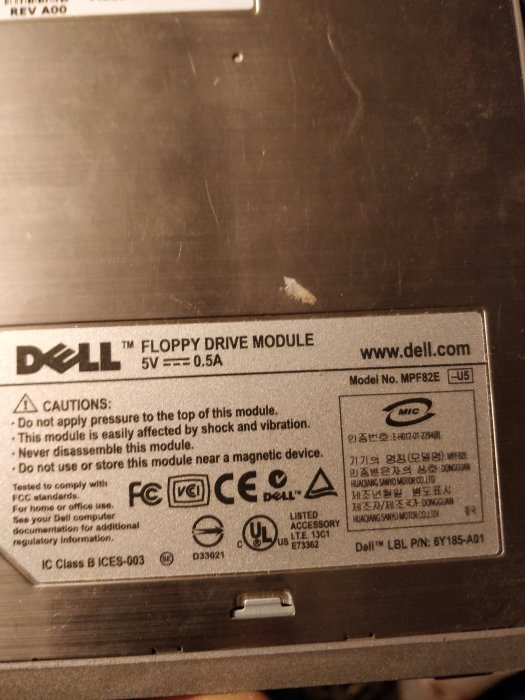 Etikett på en Dell floppy drive modul med specifikationer och säkerhetsvarningar.