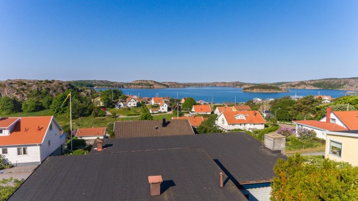 Vy över en kustby med havet i bakgrunden och traditionella hus i förgrunden under klarblå himmel.