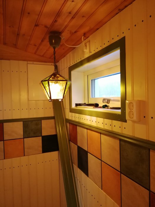 Renoverat kök med klinkergolv, träpaneler på väggarna, färgglatt kakel, och en hängande lampa.