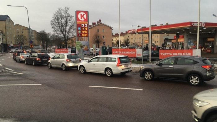 Kö av bilar som väntar vid en bensinstation med prismärkning synlig.