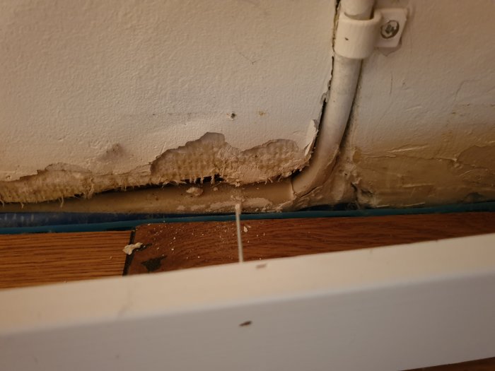 Skadad vägg med utanpåliggande vp-rör vid golvlist där kabel ska fräsas in.