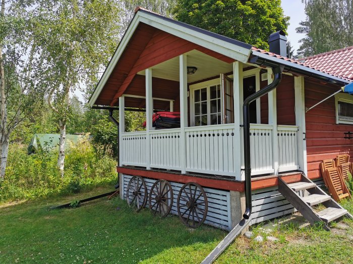Altan av ett rött fritidshus med vita staket och stolpar, behöver utvidgas, synliga plintar.