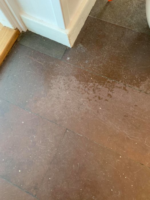 Slitet stengolv med repor och ingrodd smuts i en hall, nära en vit dörrkarm.