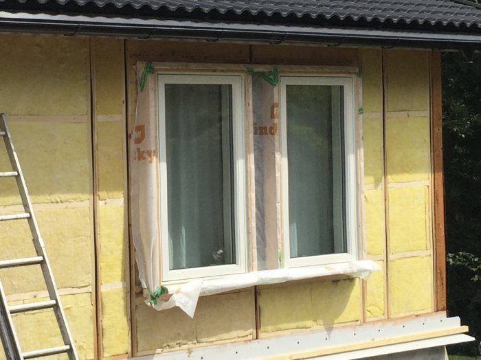 Renoverad husvägg med tilläggsisolering och utvändiga reglar runt nya fönster, med synlig vindskyddsduk.
