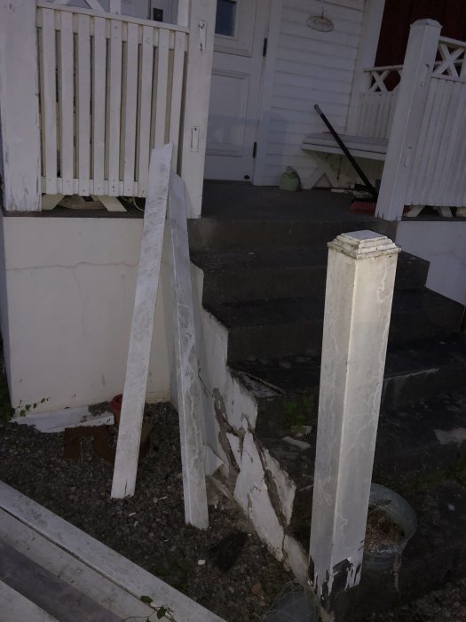 Skadade och vitmålade trästaket och betongtrappa med sprickor och flagande färg utanför en ytterdörr.