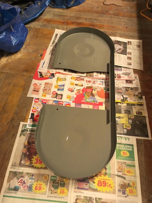 Nymålad grå skyddsplåt för bandsåg ligger att torka på ett golv täckt av tidningar.