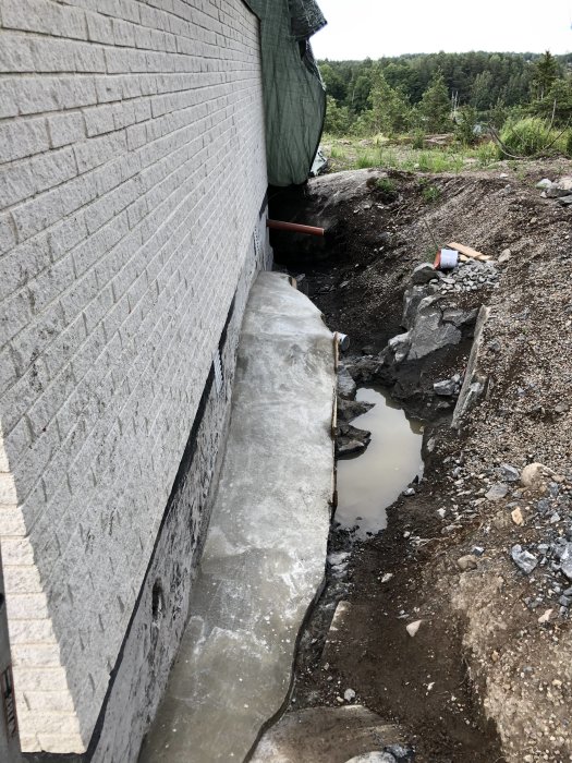 Nyggjuten ojämn och rundad betongklack vid husgrund på berg i en grävd dräneringsdike.