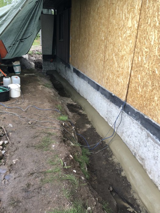 Nyggjuten betongklack vid grund av ett hus med plywoodväggar och diverse byggmaterial i förgrunden.