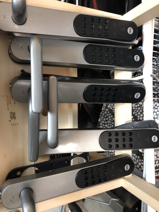 Fem Yale Doorman V2 elektroniska dörrlås staplade på en hylla, vissa med synliga repor och skav.