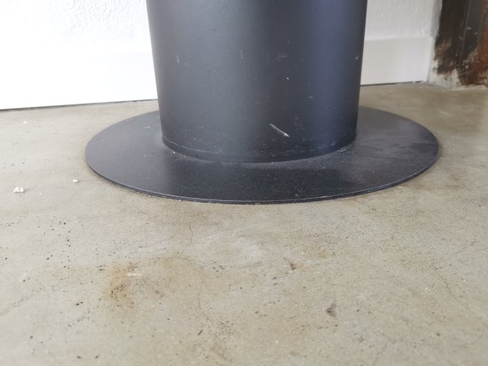 Svart fot till en Aduro 9-3 kamin på ett betonggolv nära en vägg, där ägaren överväger att kakla golvet.