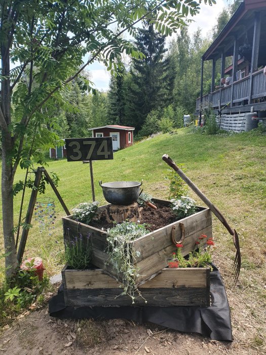 Trädgård med trädäck och planteringslåda över dold stubbe, husnummer och natur i bakgrunden.