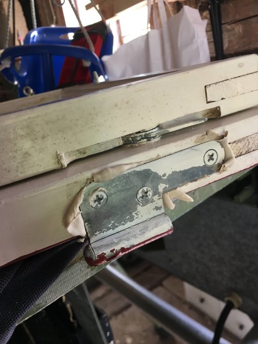 Flyttade gångjärn på ett vitt fönster med en träkloss insatt som tillfällig lösning för att minska glipan.