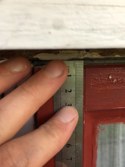 En hand håller upp ett måttband mot en fönsterkarm för att visa en glipa på några millimeter.