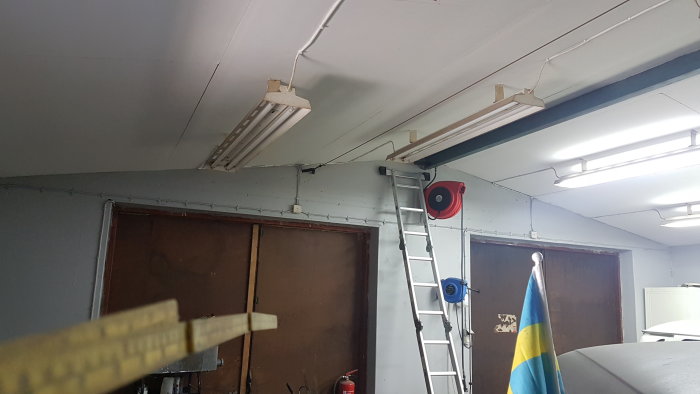 Interiör av garage med två gamla garageportar, I-balk i taket och en stege till vänster.