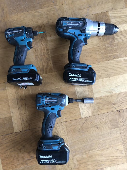 Tre olika Makita borrskruvdragare på trägolv, inklusive modeller DDF083, BHP454 och en slagskruvdragare.