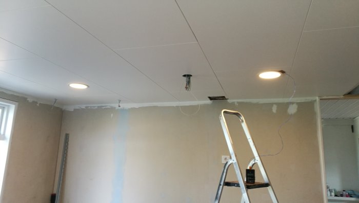 Nymålat tak med infälld belysning och stegar, pågående installationsarbete.