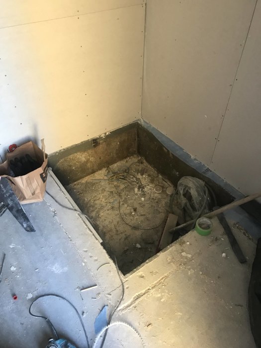 Obehandlad nisch i hörnet av ett rum med gipsväggar, redo för byggande av garderobsstomme, med byggmaterial på golvet.