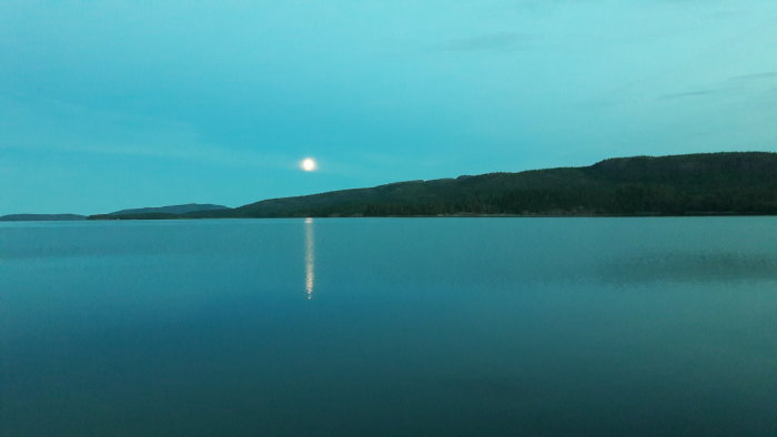 Månens sken reflekterat över en spegelblank sjö i en nationalpark innan midnatt.