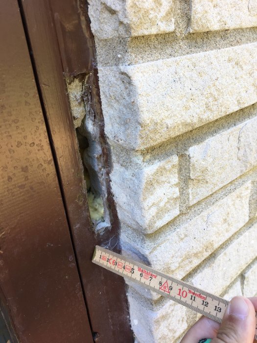 Dörrkarm med stor luftspalt mot ojämnt mexitegel och synlig drevning, mätkniv för skala.