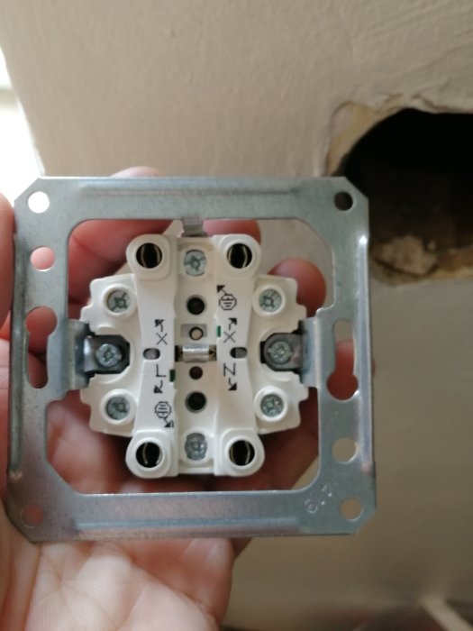Elektrisk kopplingsdosa hålls i hand framför en öppen vägg, synliga anslutningar och skruvar.