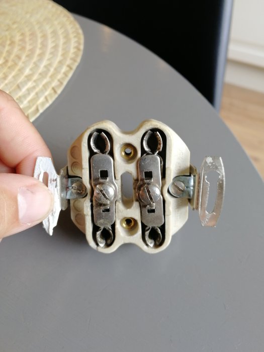 Hand håller en öppen, gammal elektrisk väggkontakt nära ett köksbord.