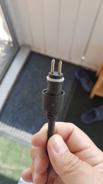 Hand håller en avklippt elektrisk kabel med en 230v till 12v transformatorplugg.