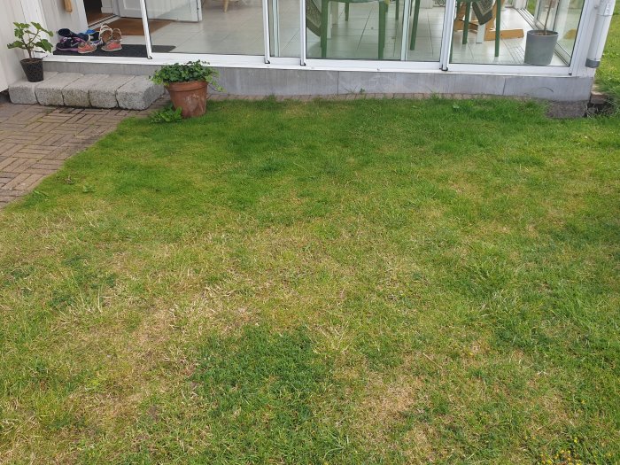 Gräsmatta med fall mot ett uterum och husgrund, visande risk för vattenintrång.