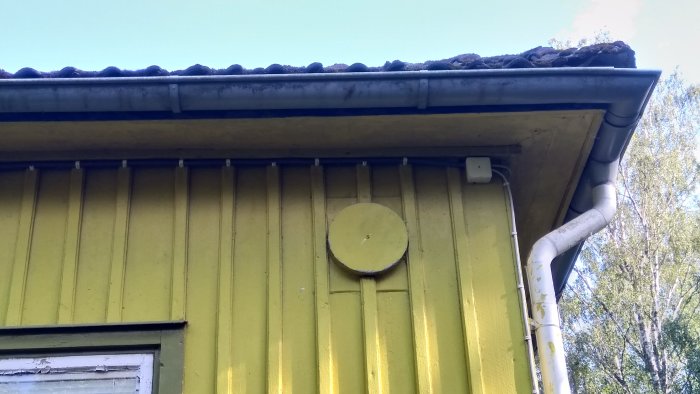 Bild av ett gult hus med en täckt rökkanalsöppning och ett rör som leder upp till takrännan.