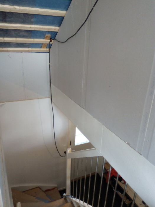 Hörnet av ett rum i ett pågående byggprojekt, där en gipsvägg möter en spånskiva nära ett trapphus.