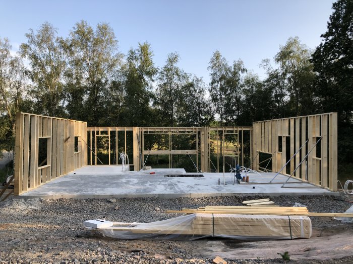 Uppförande av stommen till ett trähus med regelstommar på en betongplatta i ett omgivande grönskande område.