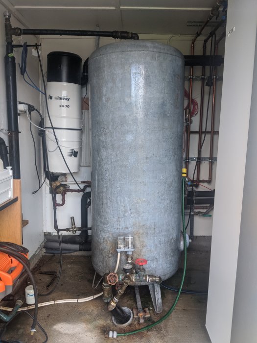 Hydrofor i pumphus med röranslutningar och automatisk avluftare synlig.