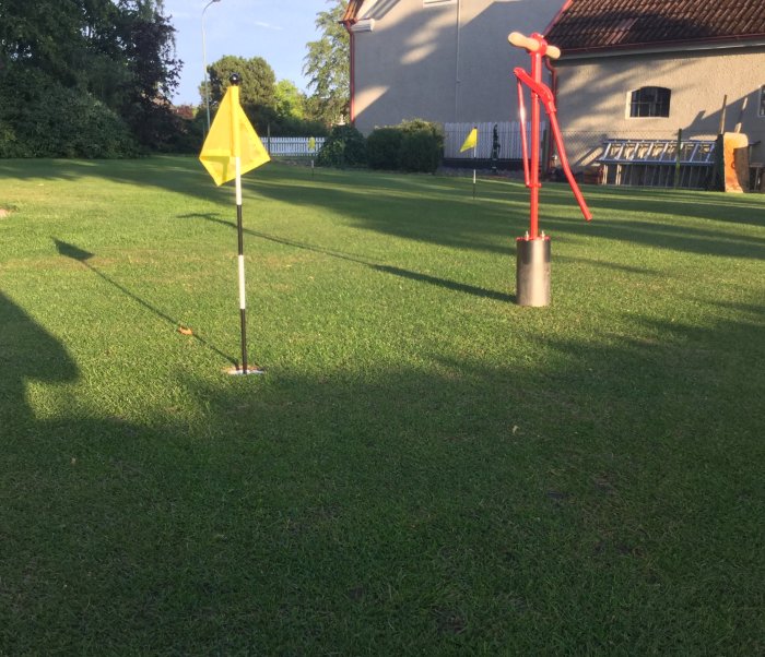 Gul hörnflagga på fotbollsplan med röd vattendunk som målnätstöd i bakgrunden och gräs i förgrunden.
