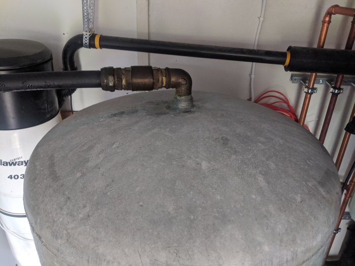Översikt av en hydrofor med rörkopplingar och ventiler på toppen i ett pannrum.
