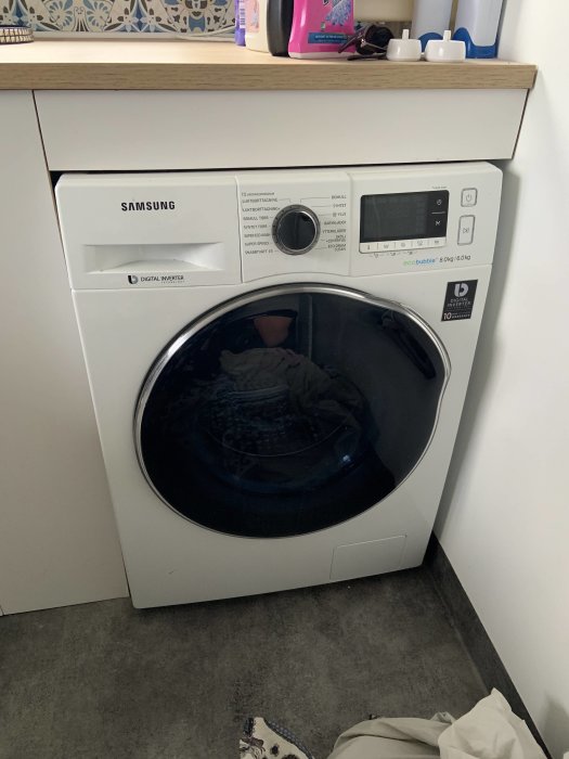 Samsung Eco Bubble tvätt-/torkmaskin under bänk med kontrollpanel och tvätt inuti.