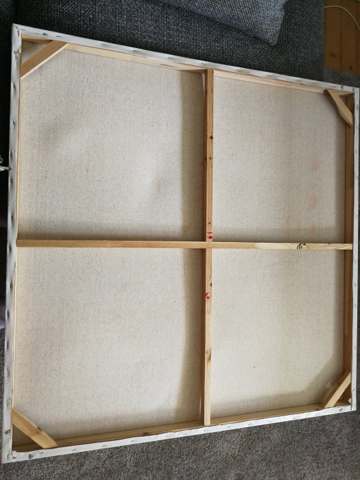 Baksidan av en tavla utan beslag, med synlig träram och mittenstöd på en matta.