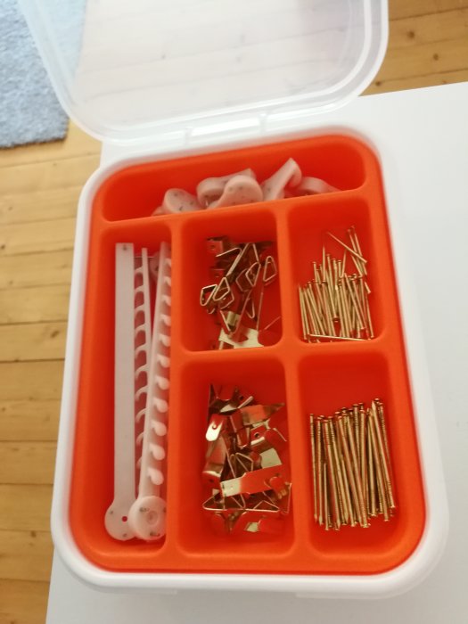 Organiseringslåda med bildupphängningsmaterial som spik, hängare och skruvpluggar.