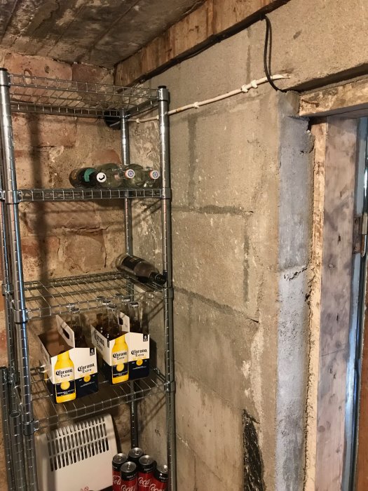 Bild på skadat tegel och betongväggar i källare med hyllor innehållande drycker och en gammal dörr.