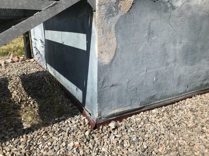 Närbild på en husgrund med spruckna och slitna betongväggar samt grusmark runtomkring.