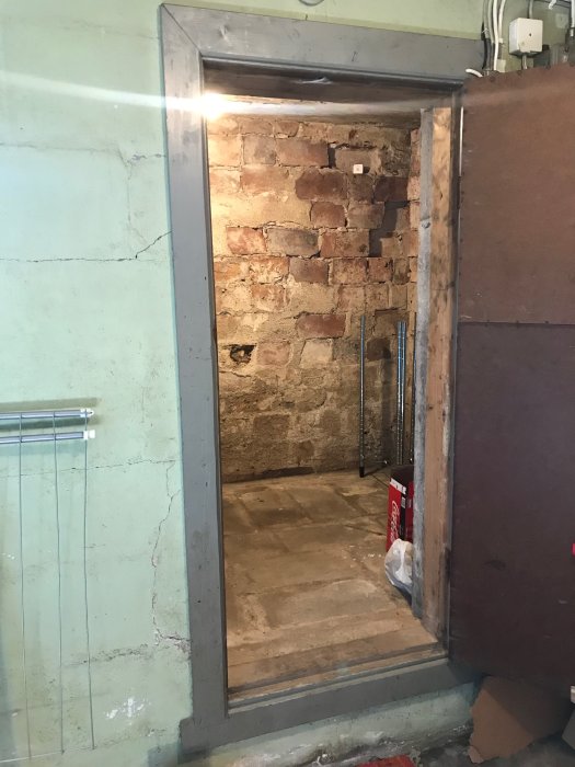 Öppning till ett potatiskällarutrymme under renovering, med skadade tegelväggar och betonggolv.