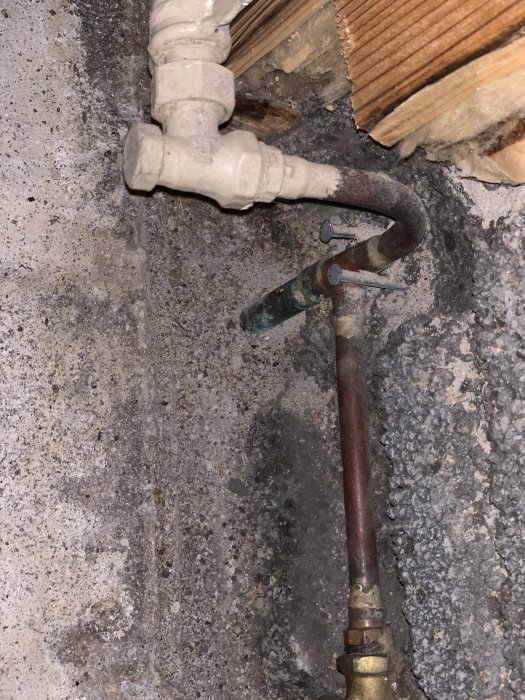 Stålrör och kopparledning med ventil och lekande mutter i en betongmiljö, indikation på renoveringsarbete.