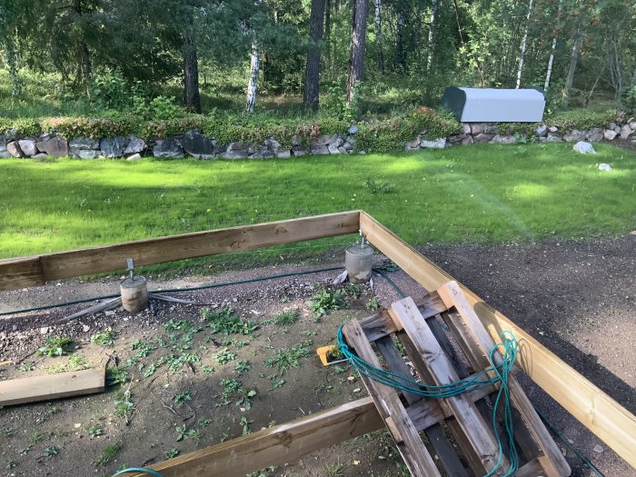 Nyplanterat område till höger, äldre gräsområde till vänster med stenmur och skog i bakgrunden.