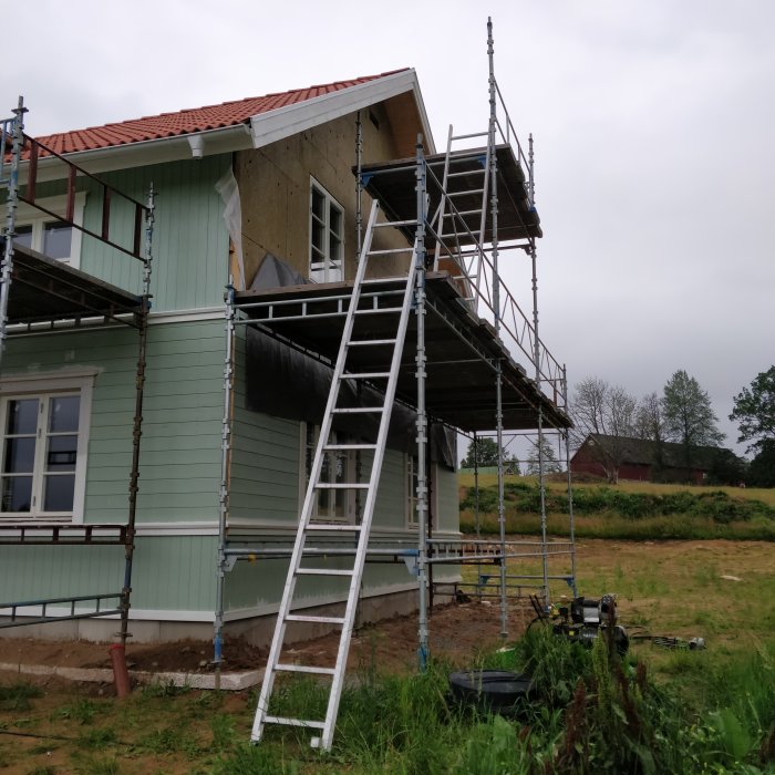 Renovering av hus med delvis monterad stående och liggande panel och byggnadsställningar.