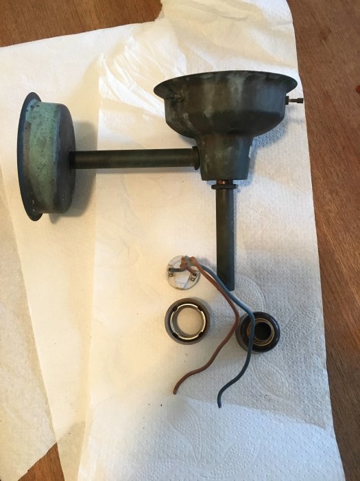 Nedmonterad taklampa med koppartrådar och monteringsdetaljer på en yta täckt av hushållspapper.