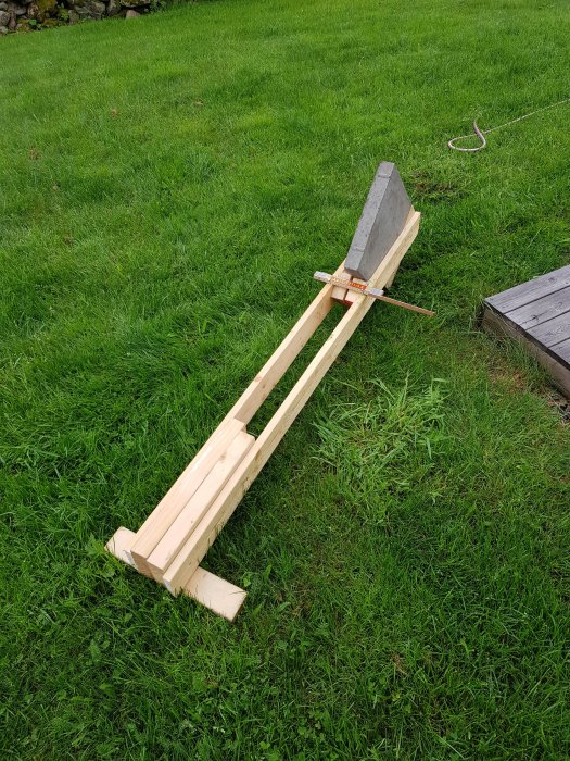 Hemmagjord apparat för nedgrävning av kabel i trädgård med träram och betongvikt.