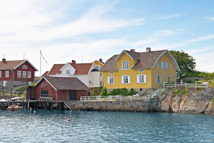 Traditionella svenska hus vid vattenkanten med en brygga och en svensk flagga som vajar.