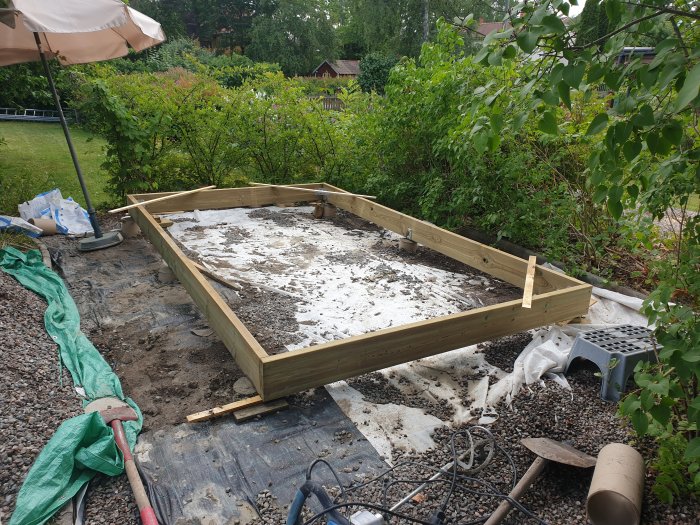 Nybyggd trädgårdsgrund av tryckimpregnerat trä 195x45 på vit täckduk med trädgårdsverktyg runtom.