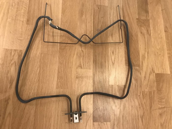 Defekt ugnselement från en IKEA REALISTISK ugn som ligger på ett trägolv.