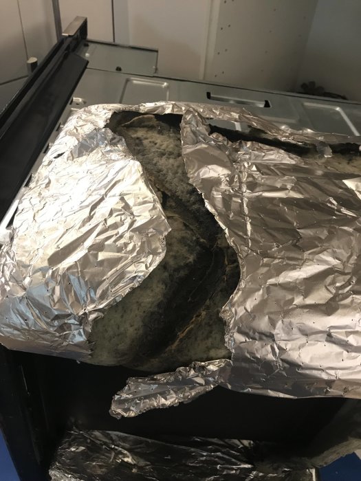Damaged oven insulation with exposed mineral wool and torn aluminium foil.