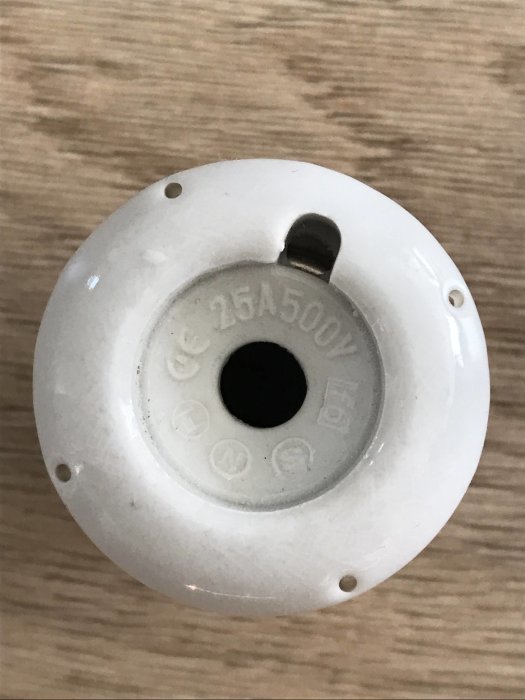 Vit keramisk elektroinstallation med märkningen "25A 500V" på en träyta.