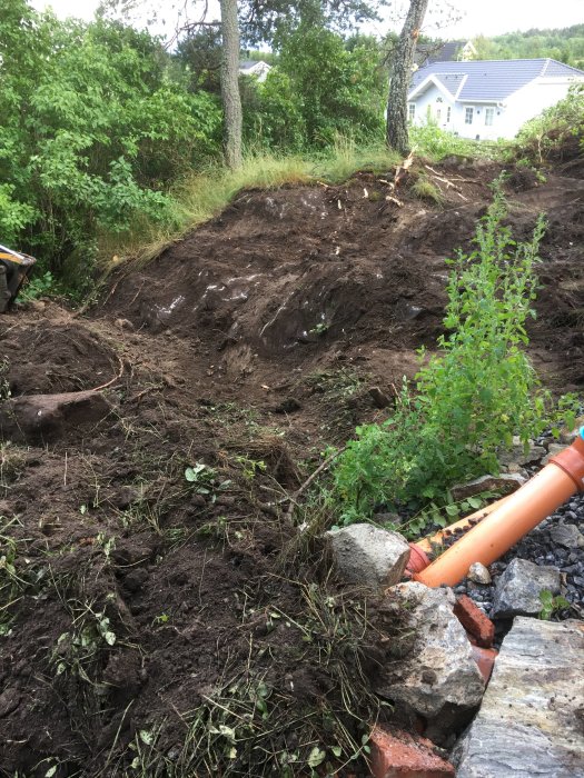 Grävd slänt som visar berget för planering av pool med hus och grönska i bakgrunden.